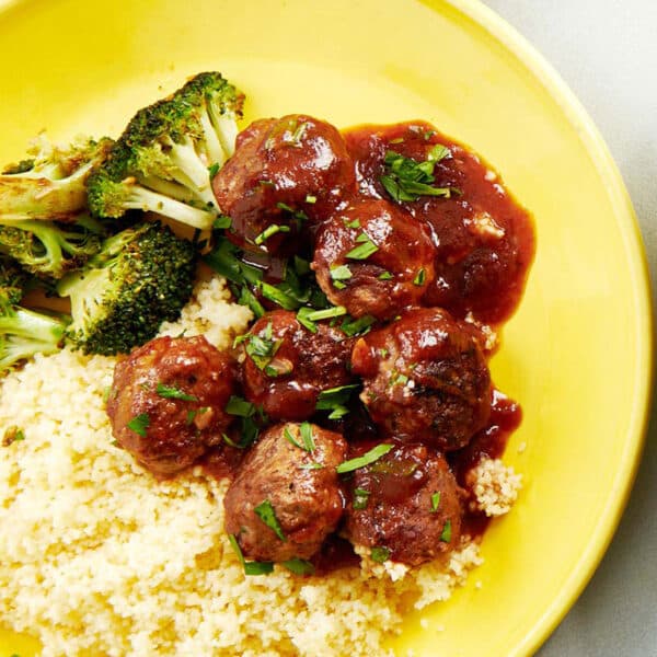 Sweet and sour meatballs over rice on yellow plate.