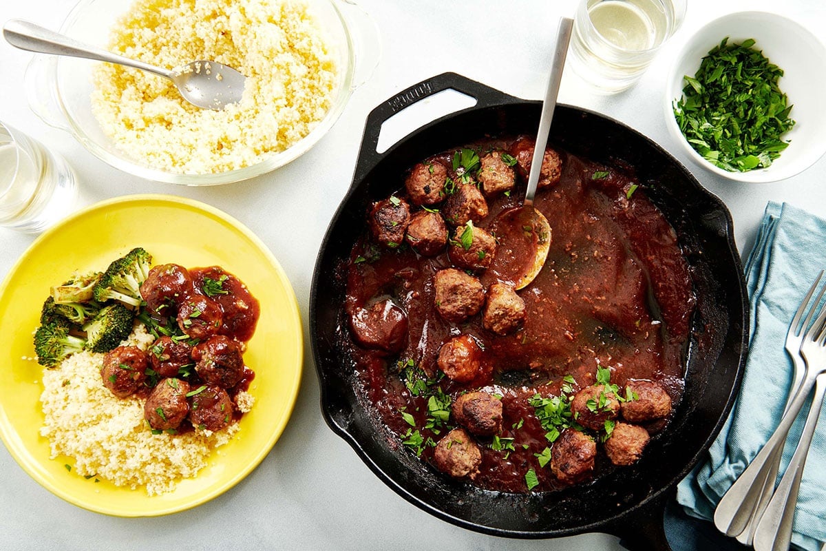 Skillet of Sweet and Sour Meatballs on a table with meatballs on yellow plate with rice and broccoli.