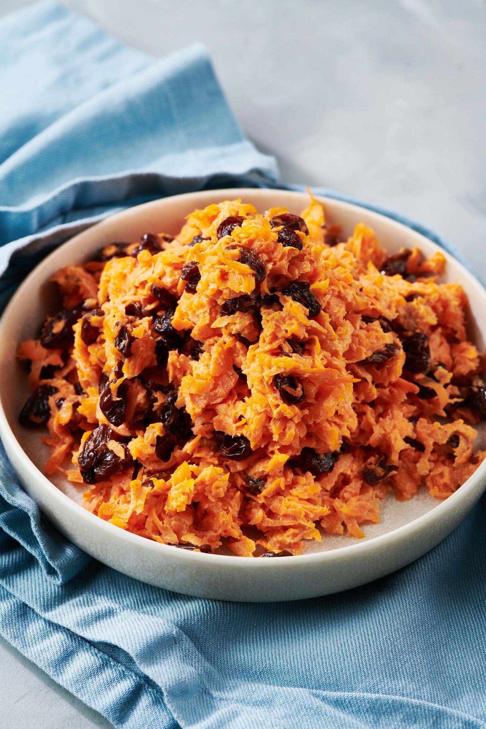 Bowl of Carrot Raisin Salad on table with blue napkin.