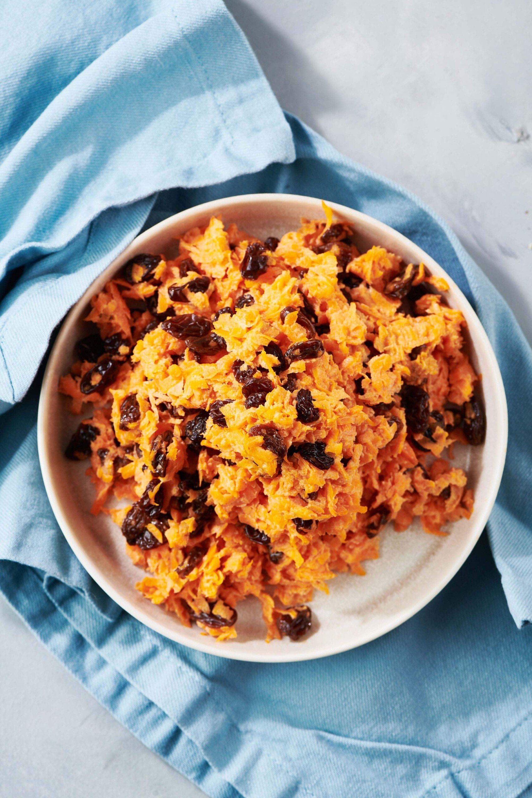 Carrot Raisin Salad in white bowl with blue napkin.