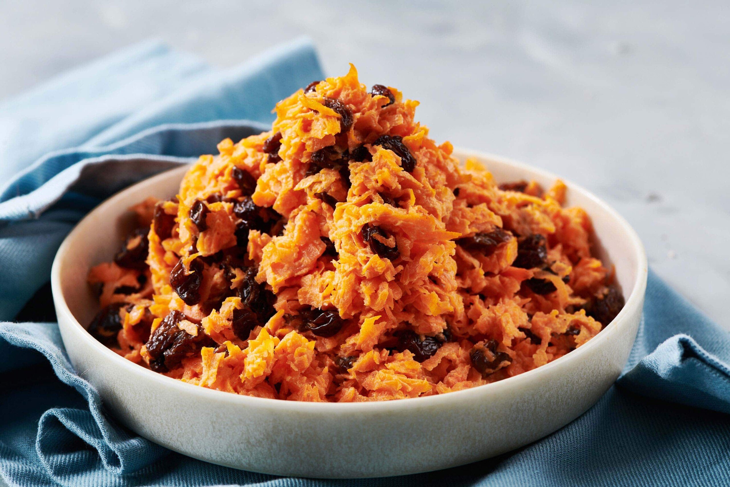 White bowl filled with Carrot Raisin Salad on blue napkin.