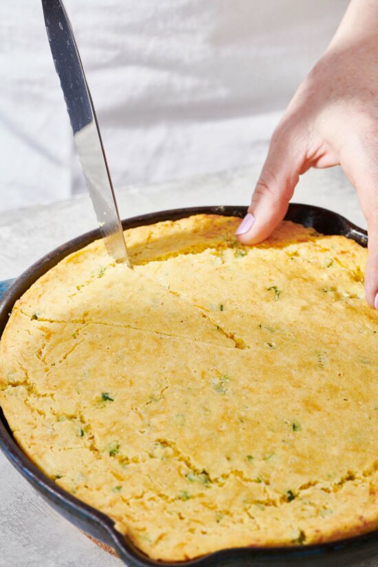 Woman slicing Cheddar Jalapeno Cornbread in a cast iron skillet.