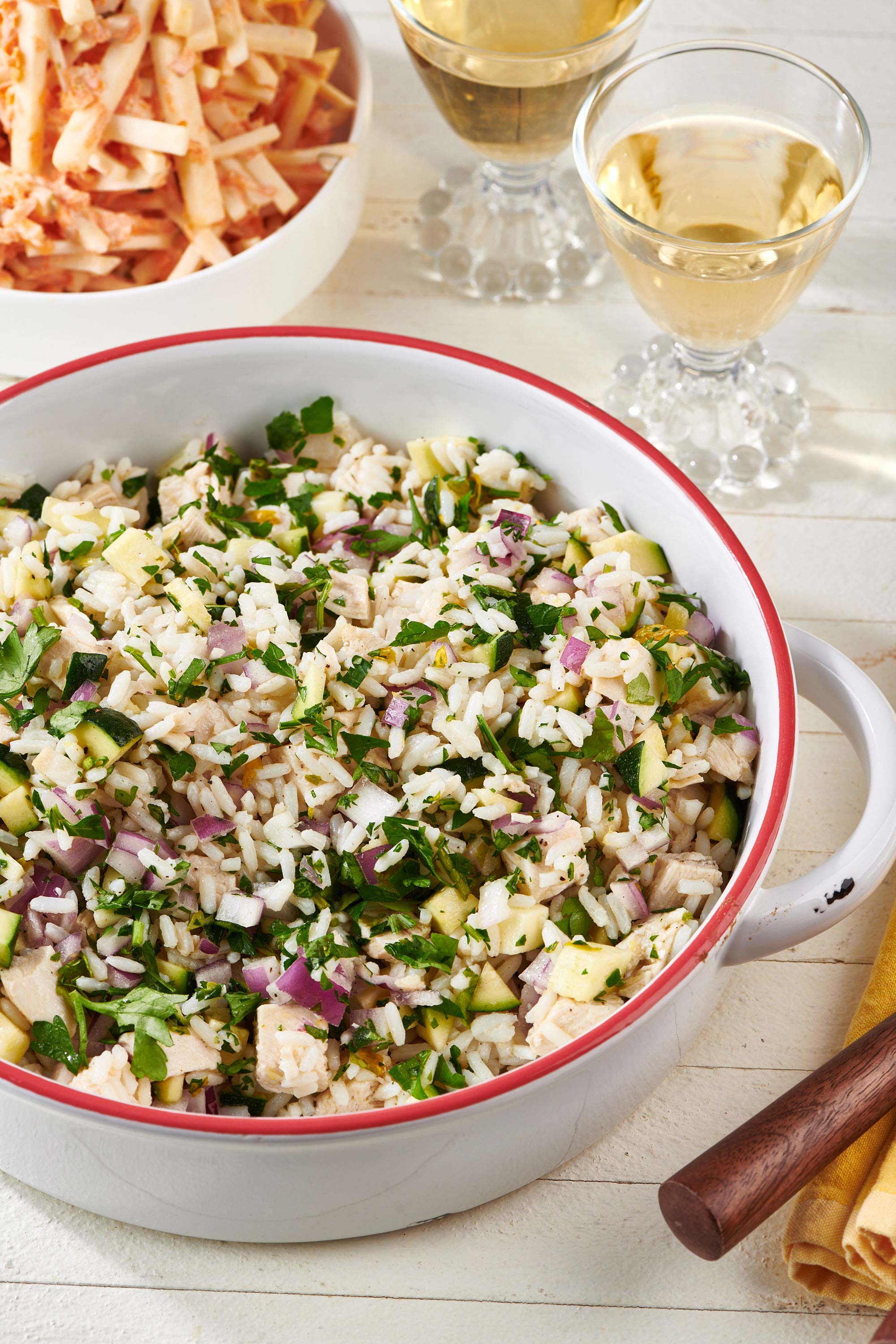 Chicken and Rice Salad in a serving bowl with two glasses of white wine and celeriac salad.