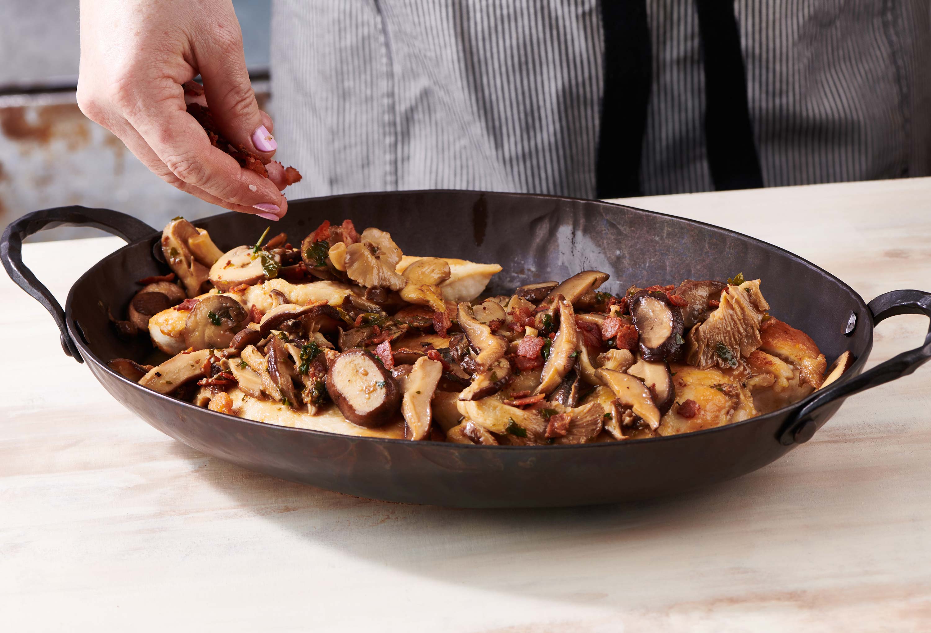 Woman sprinkling pancetta over a dish of Chicken Marsala.