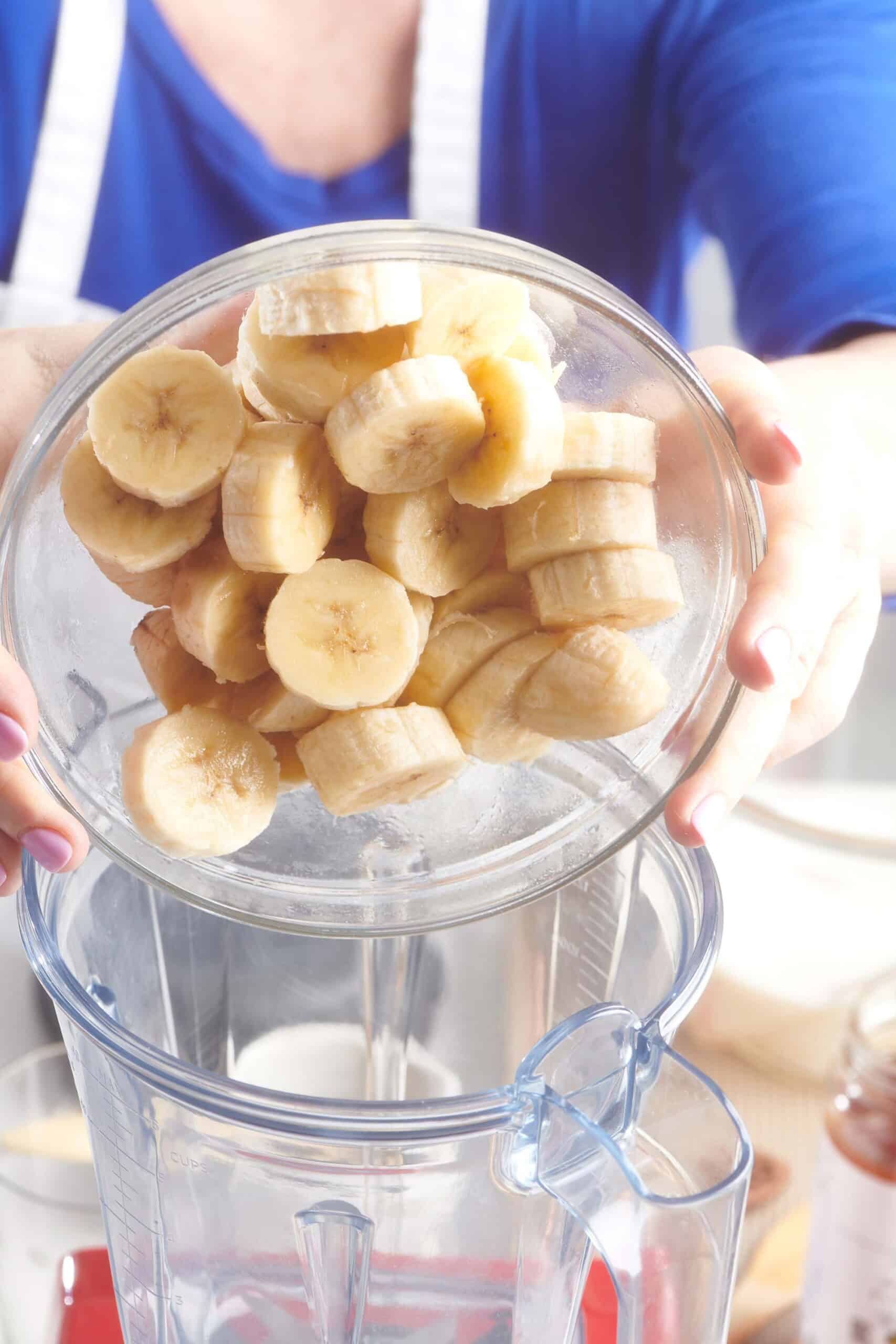 Woman pouring banana slices into a blender.