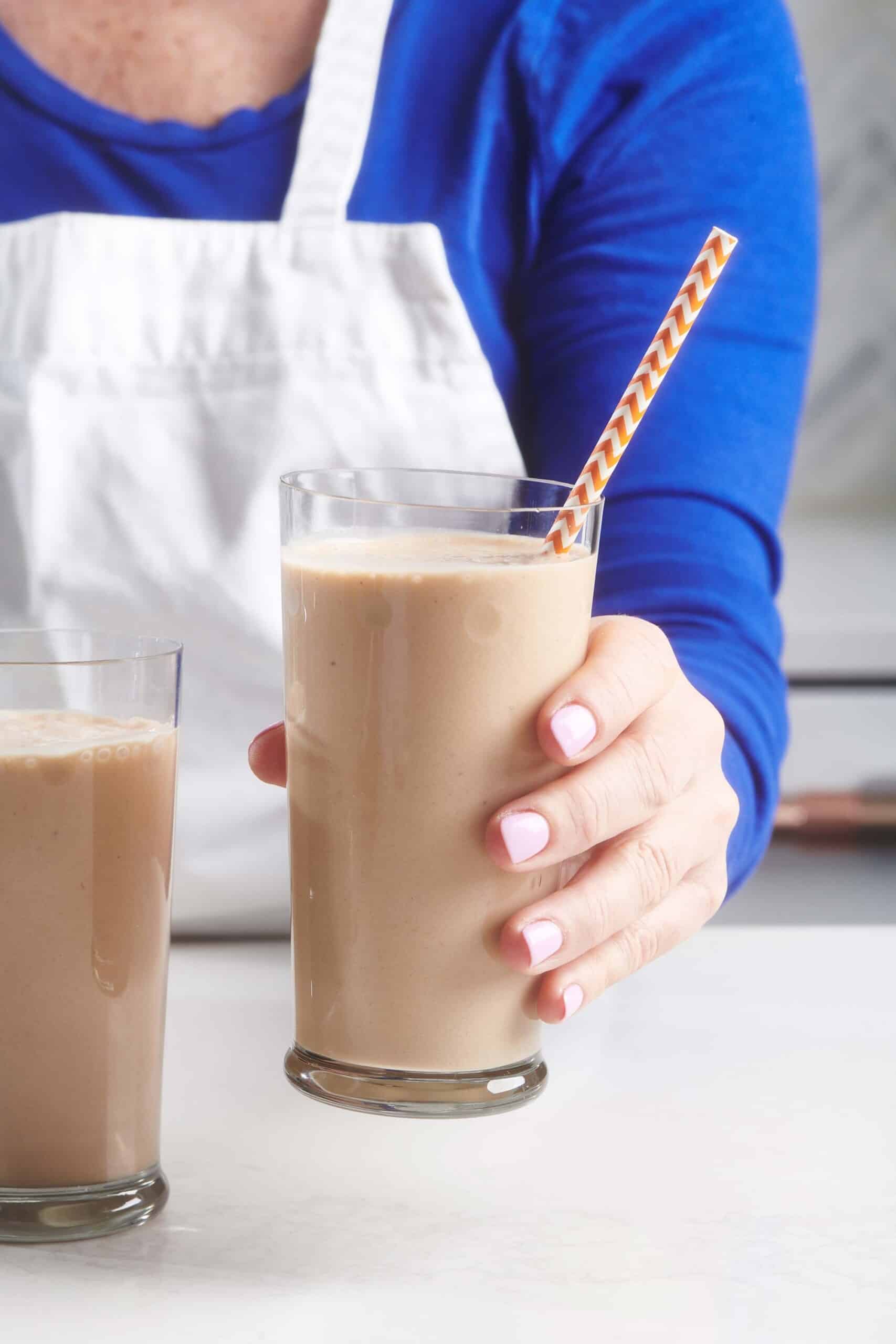 Woman holding a Chocolate, Peanut Butter and Banana Smoothie in a tall glass.