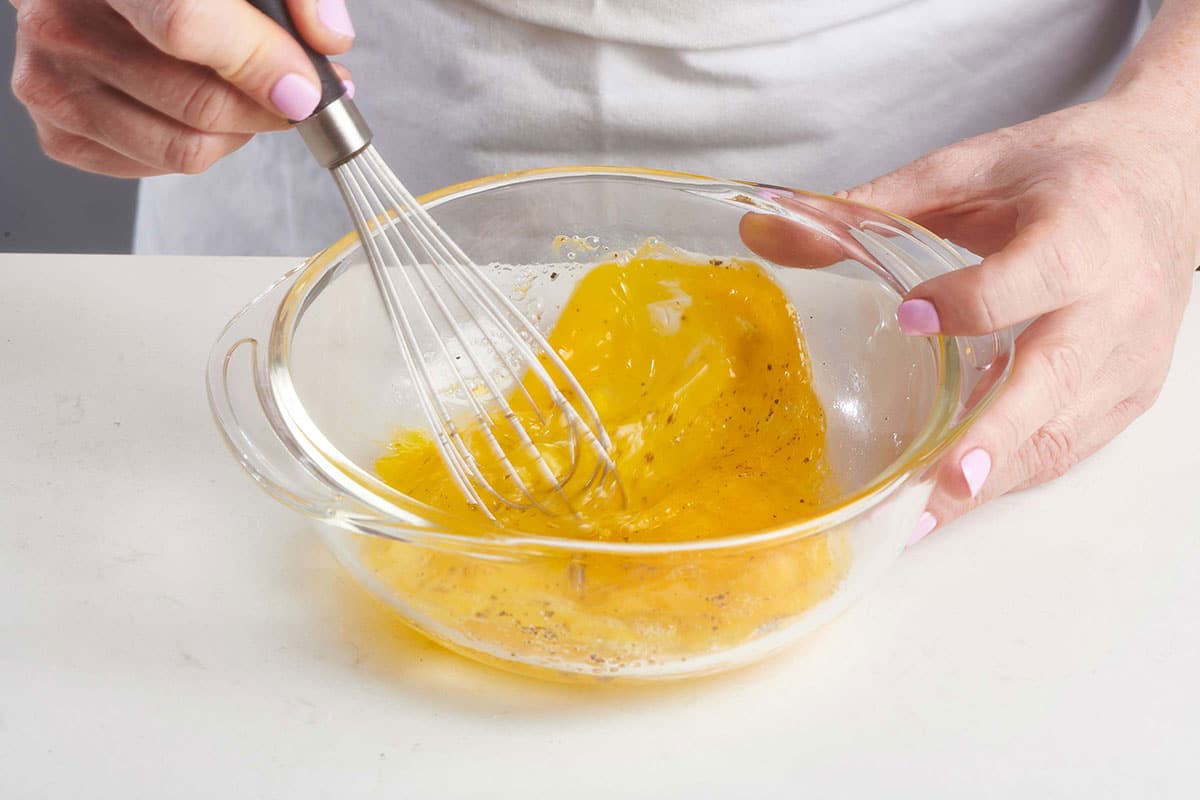 Woman whisking eggs in a glass bowl.