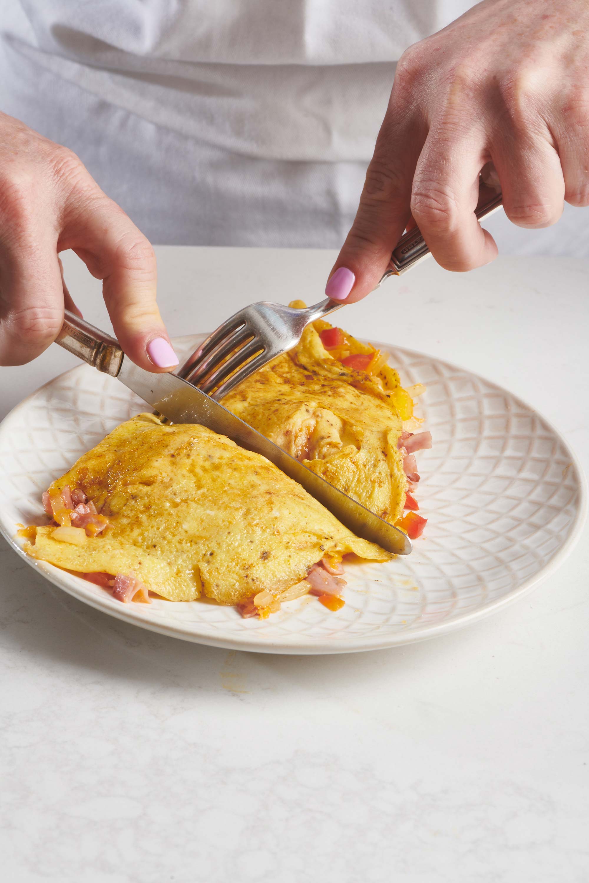Woman cutting a Denver Omelet with a knife.