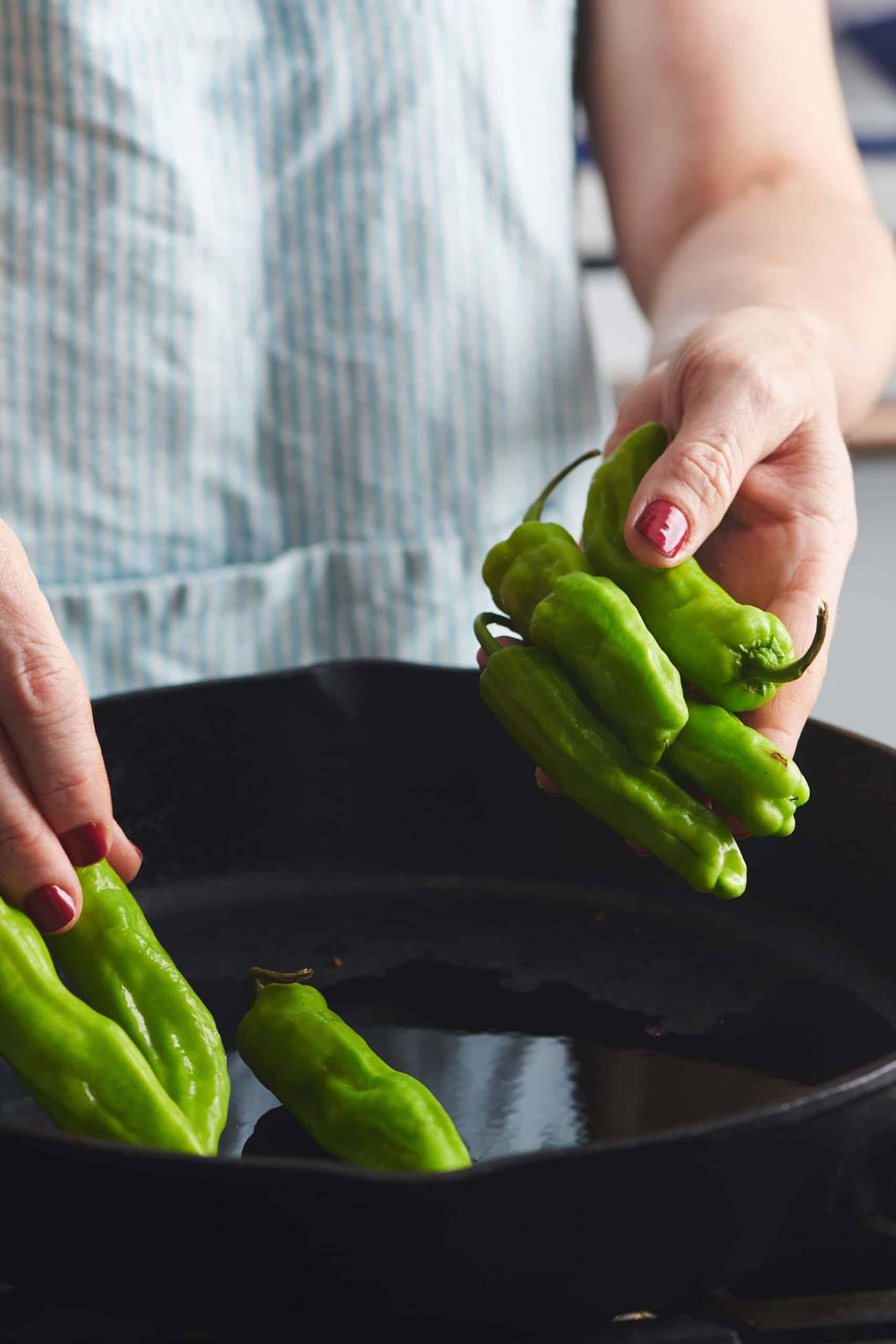 Woman putting Shishito Peppers into a skillet.