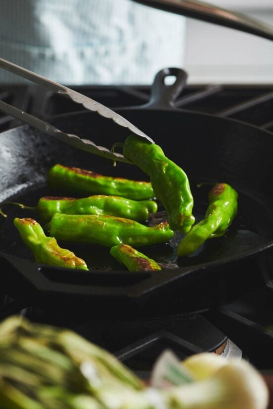 Tongs flipping a Shishito Pepper in a skillet.