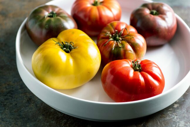 A variety of heirloom tomatoes ripening on white plate.