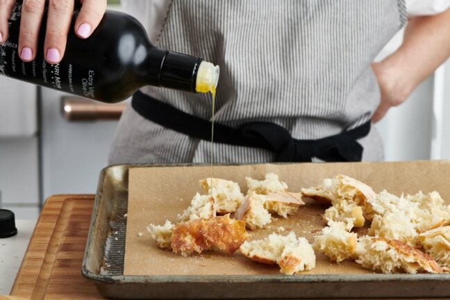 Woman pouring olive oil onto torn pieces of bread.