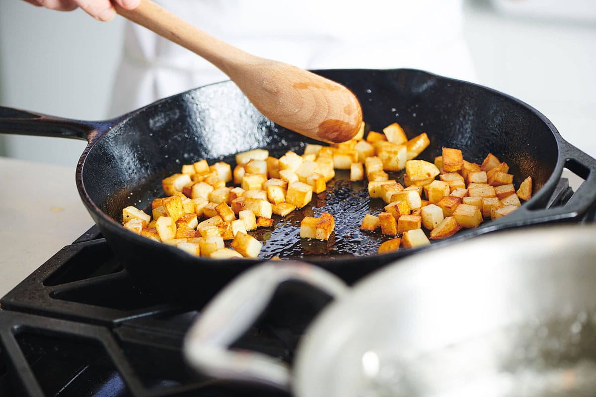 Cooking diced potatoes in cast iron pan on the stove.