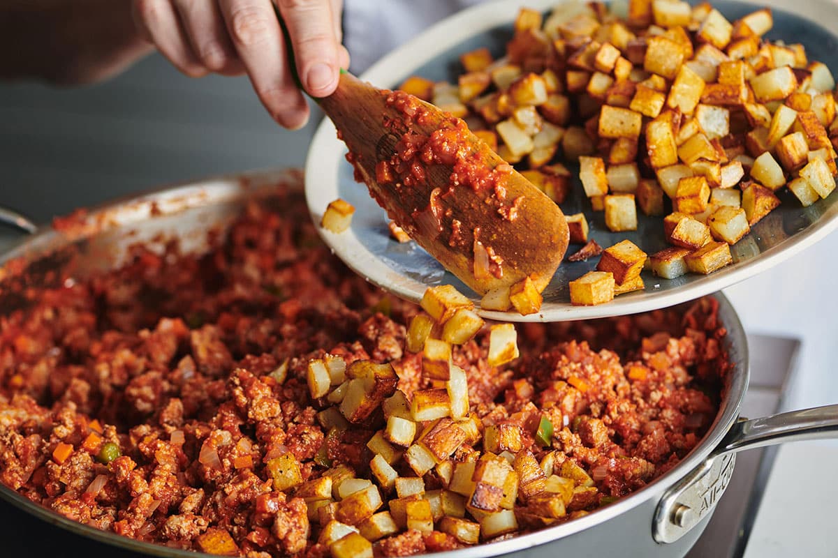 Woman stirring crispy potatoes into a skillet of Turkey Picadillo.