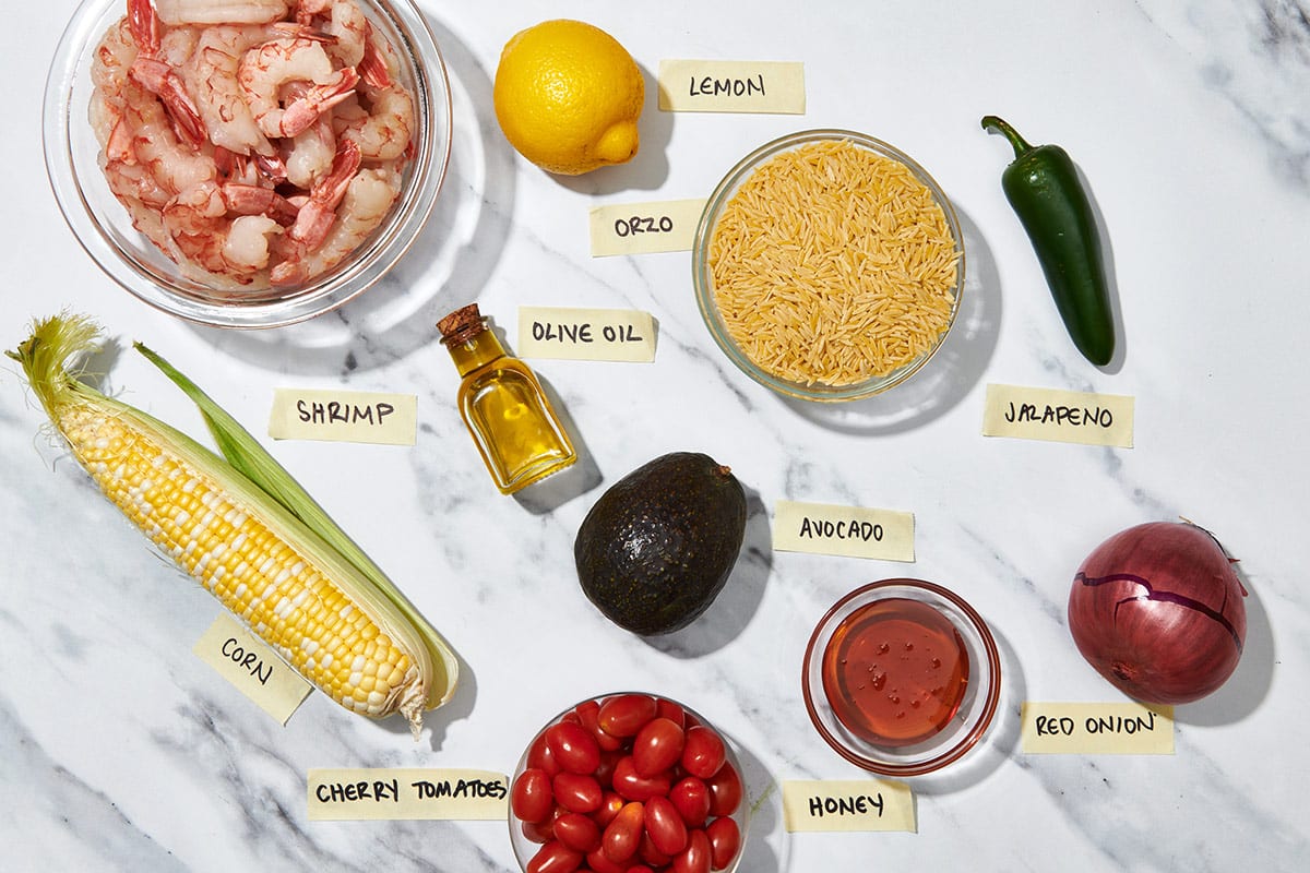 Shrimp, orzo, corn, and other ingredients for salad on marble.