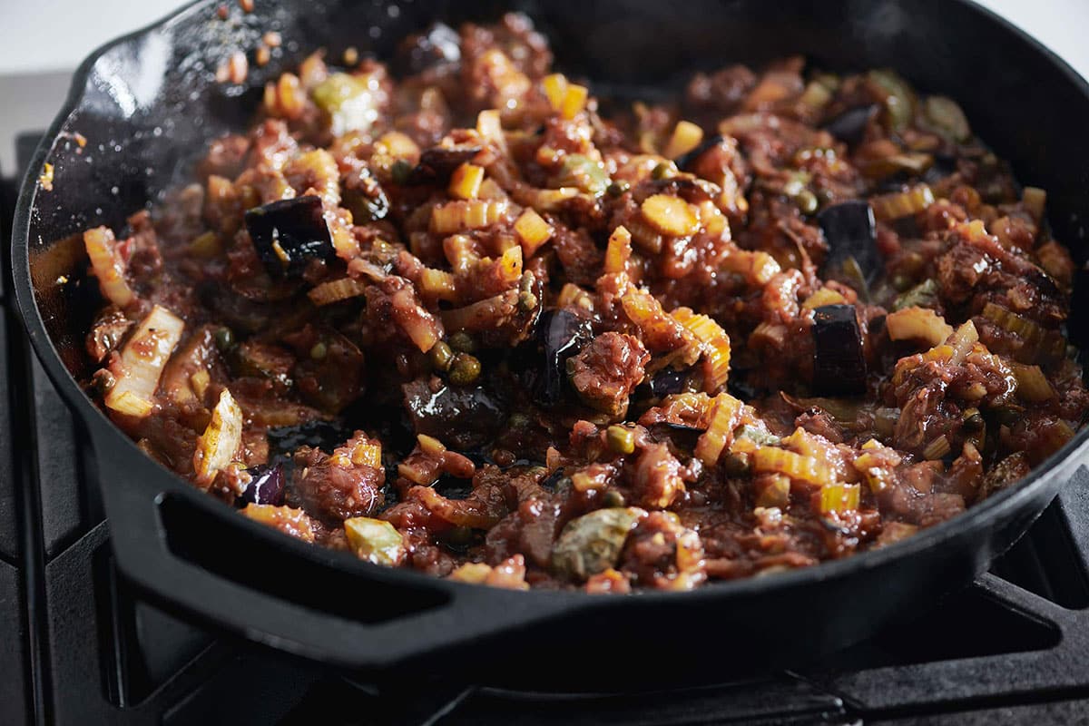Caponata in a black skillet on stove.