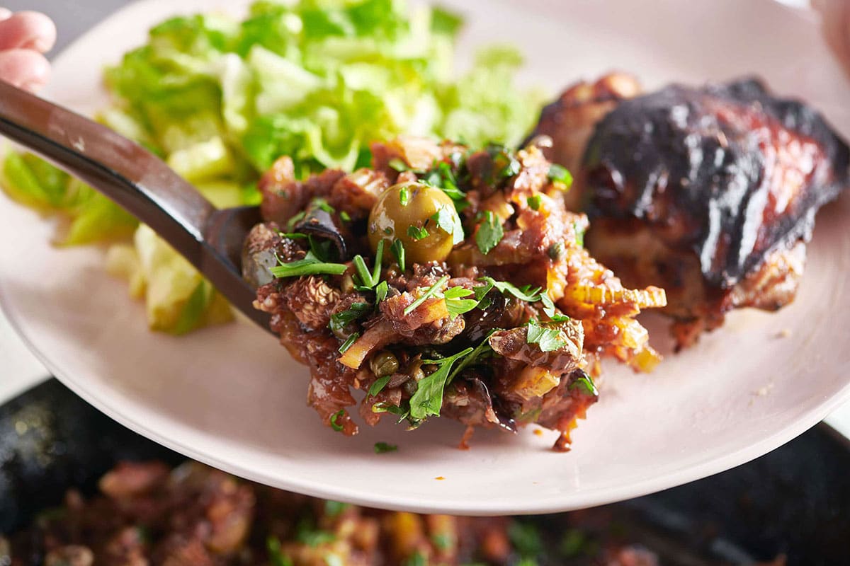 Serving caponata on plate with chicken and salad.