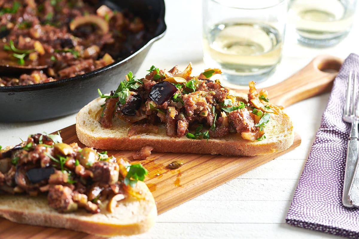 Two pieces of Caponata bruschetta on wood board.