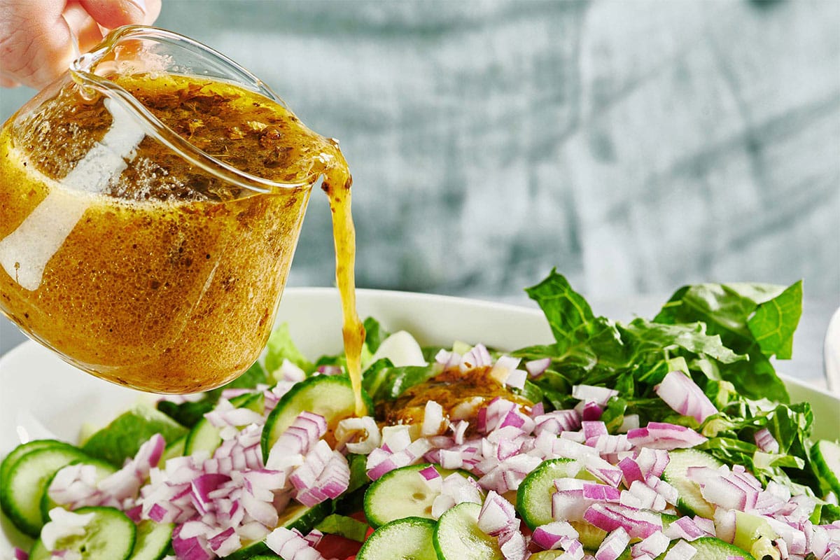 Pouring vinaigrette over Greek salad in serving bowl.