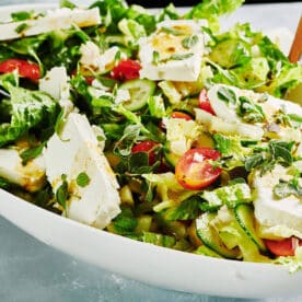 Greek salad with feta cheese in white serving bowl on table.