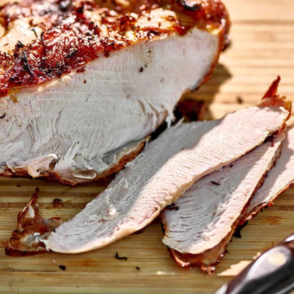 Sliced grilled turkey breast on cutting board with knife.