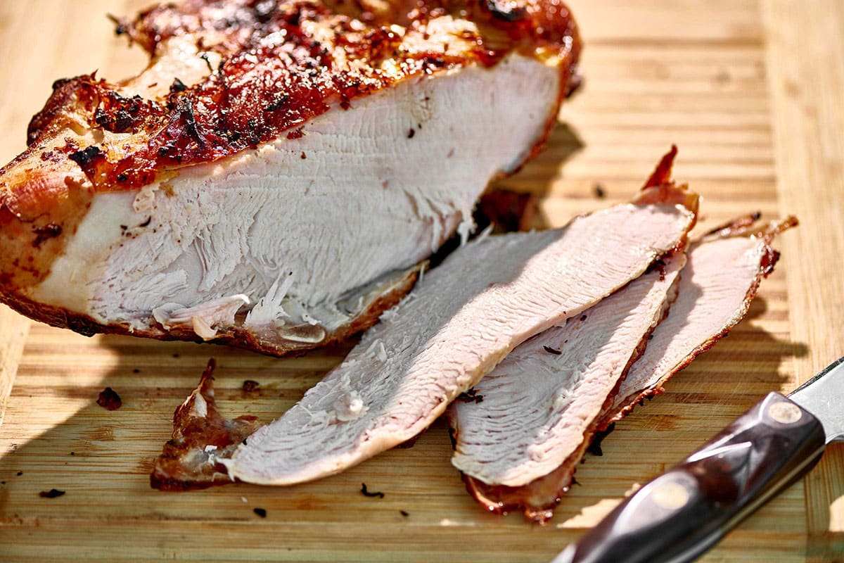 Sliced grilled turkey breast on cutting board with knife.