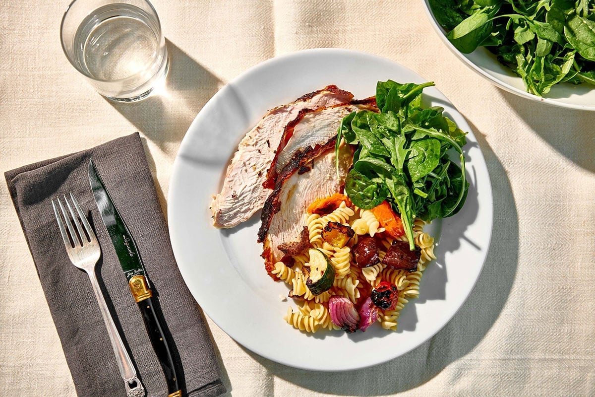 Plate of Grilled Split Turkey Breast, greens, and pasta salad.