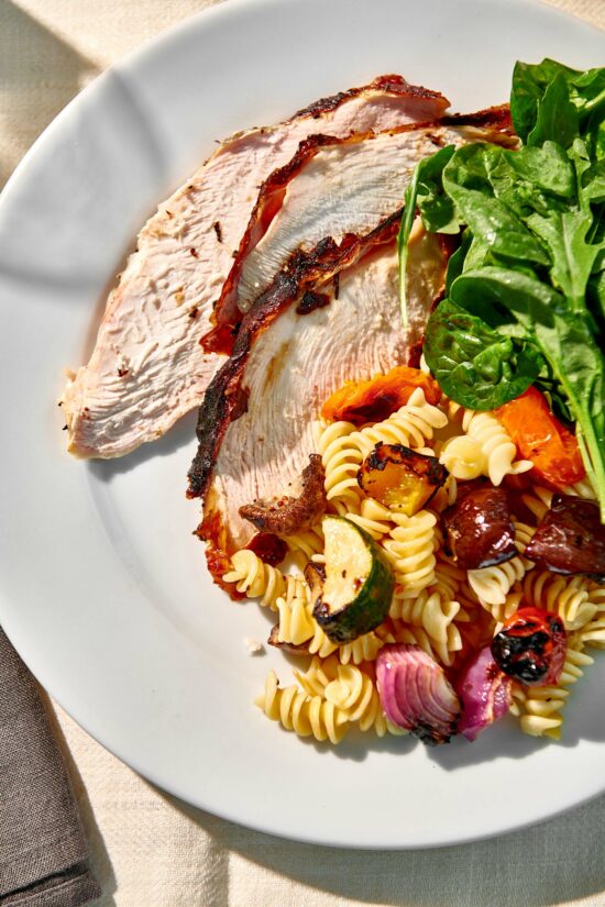 Slices of Grilled Split Turkey Breast on a plate with pasta salad and greens.