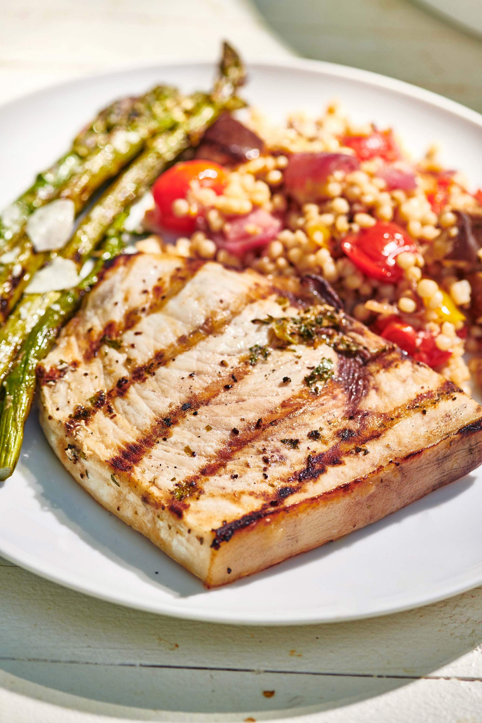 Swordfish with grill marks on a plate with asparagus and grain salad.