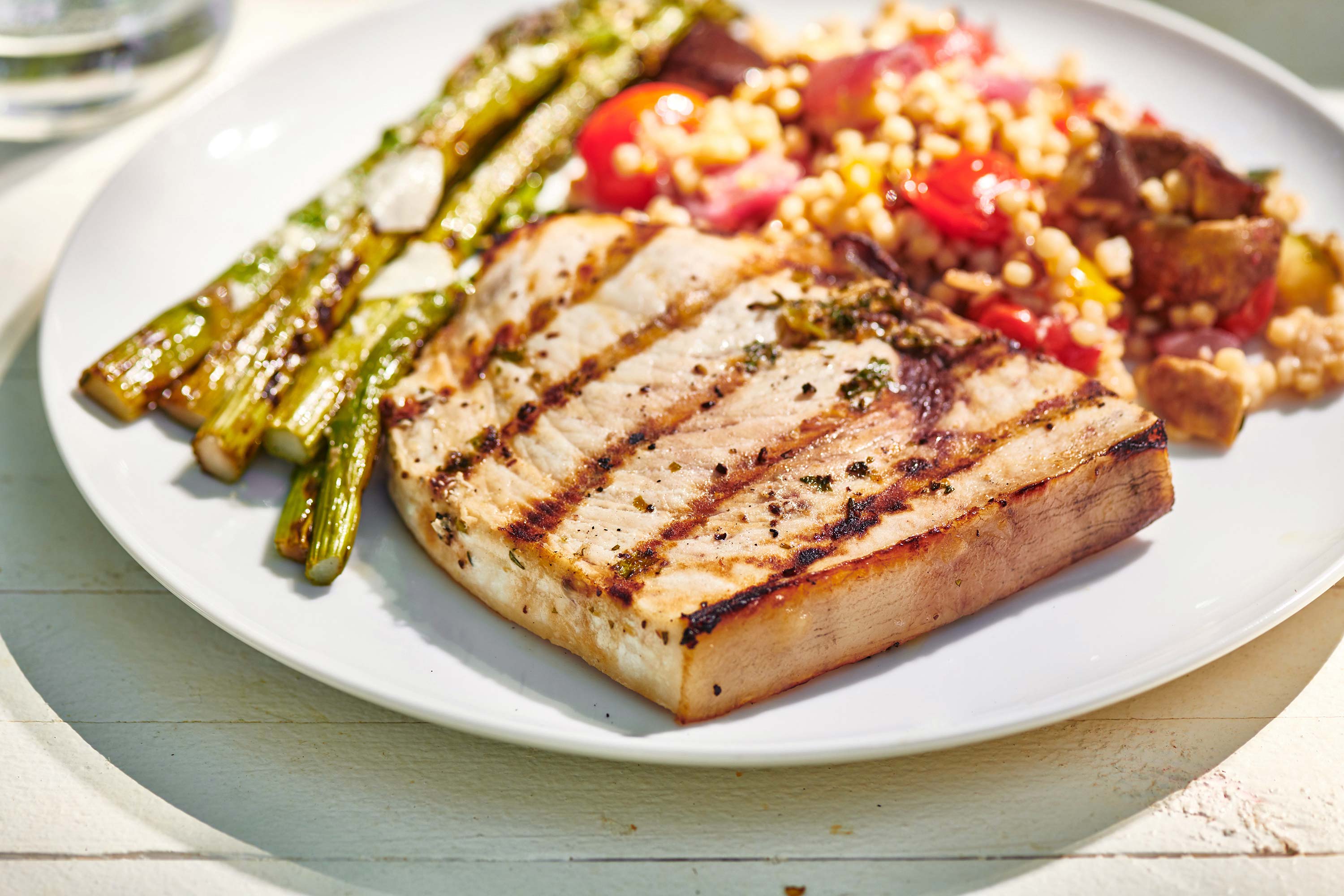 Grilled Swordfish with asparagus and couscous salad on a white plate.