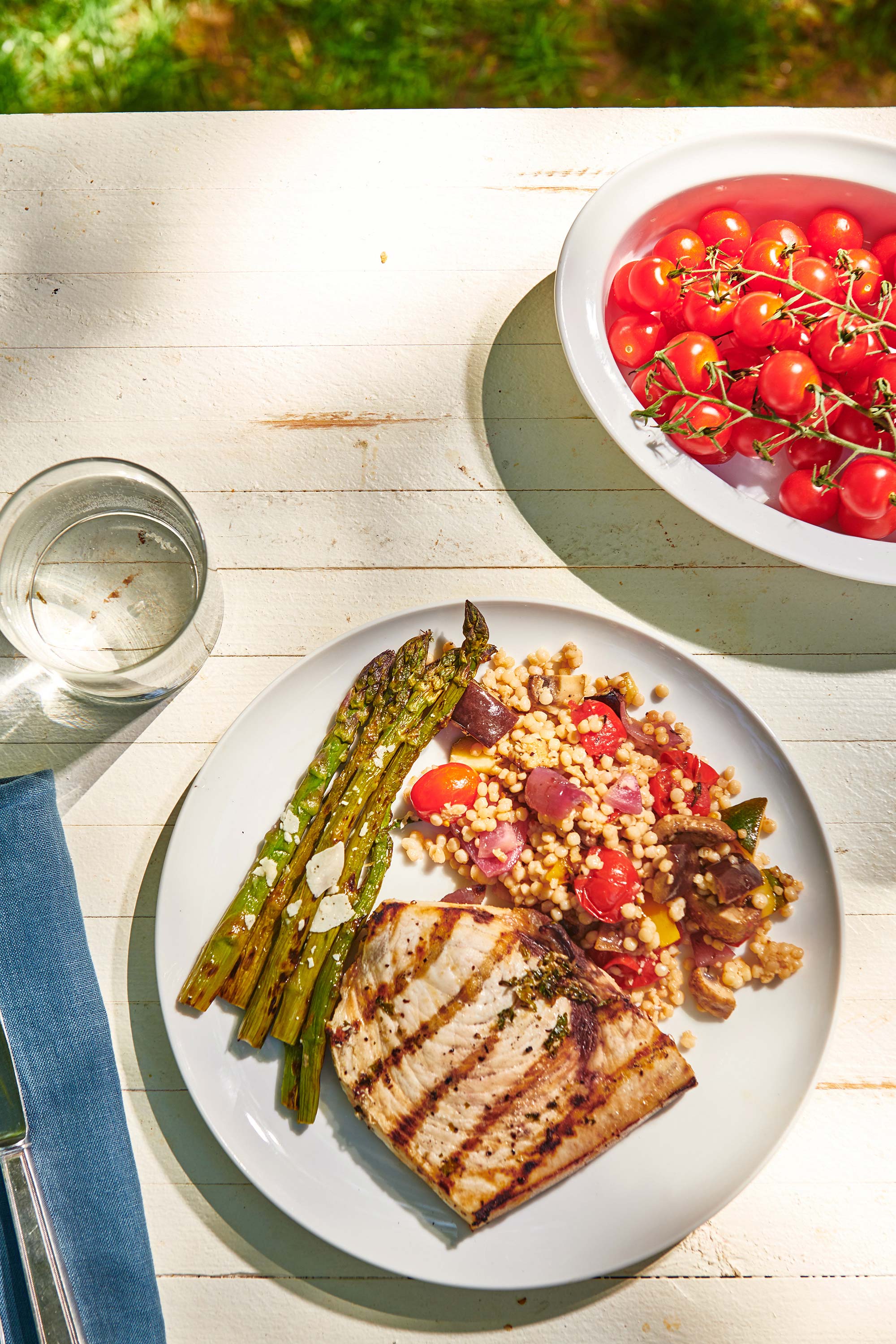 Plate of swordfish, asparagus, and grain salad on a white, wooden table.