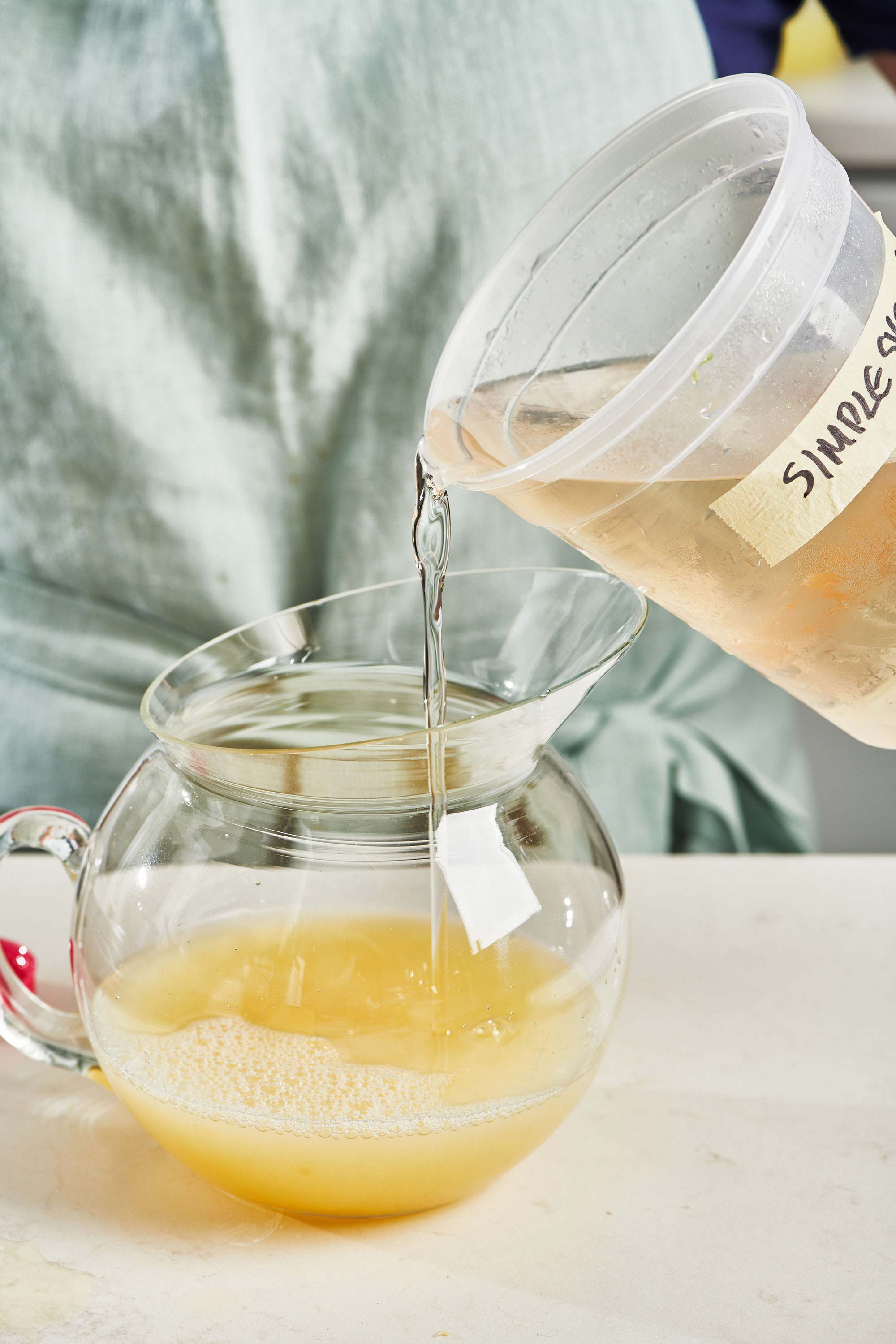 Simple syrup pouring into a pitcher of lemon juice.