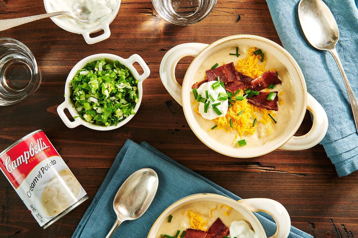 Bowls of Loaded Baked Potato Soup on a table with a can of Campbell's cream of potato soup.