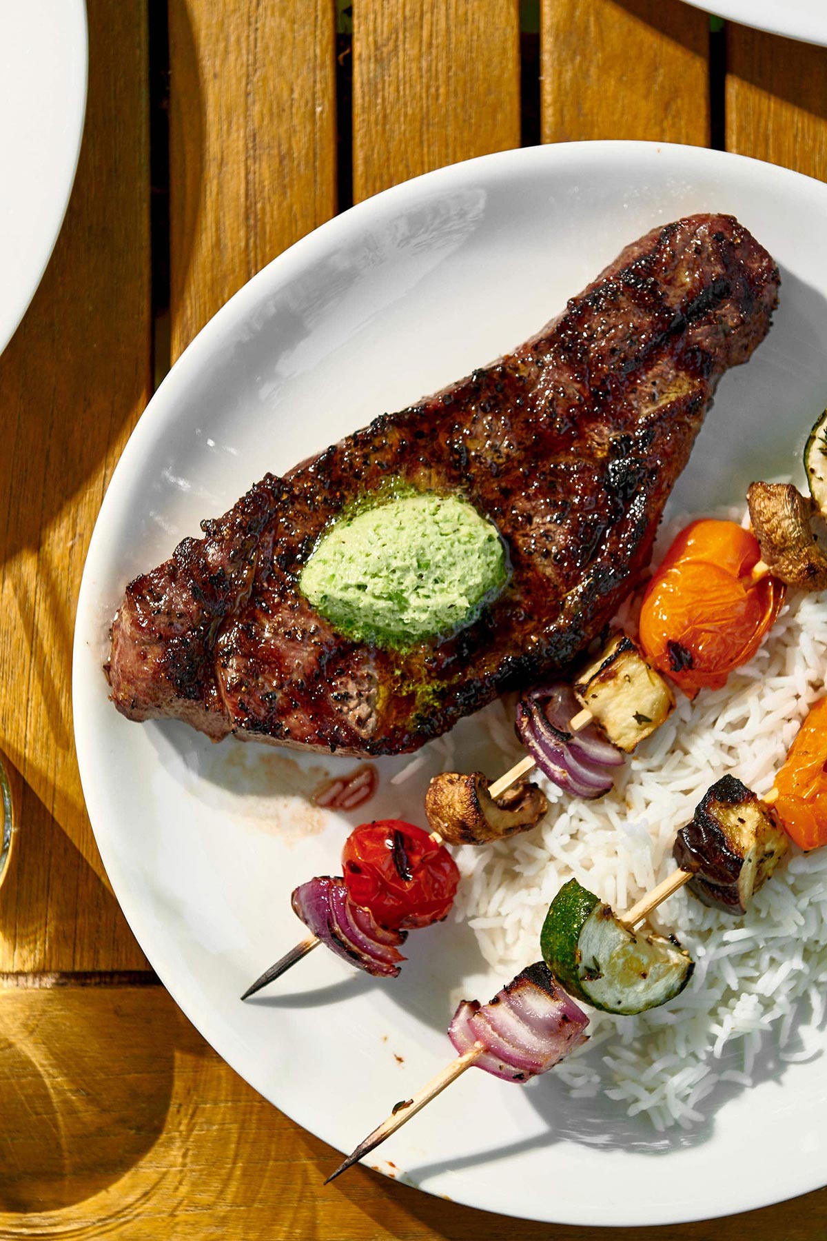 Veggie kebabs, rice, and New York Strip Steak with Jalapeno Butter on a white plate.