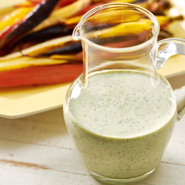 Homemade creamy cilantro sauce in jar next to roasted carrots.