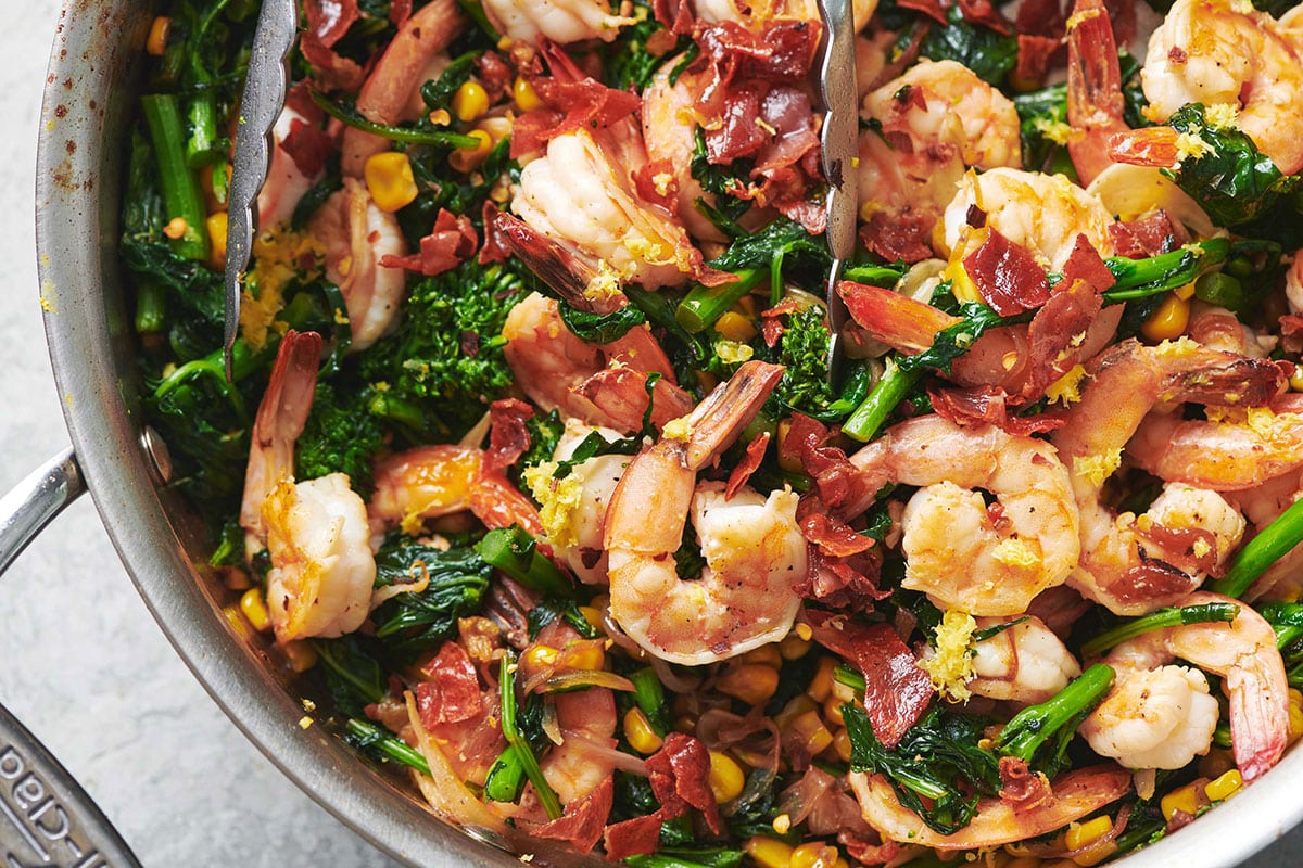 Sauteed Shrimp with Vegetables topped with prosciutto in a skillet.
