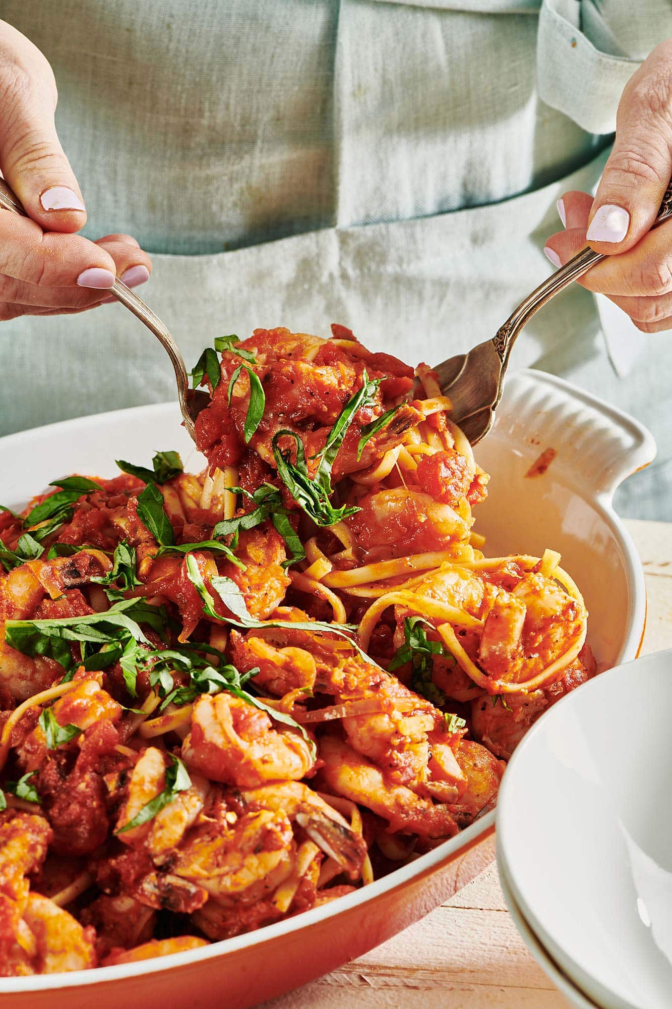 Woman serving up Shrimp Fra Diavolo with Linguine from white serving dish.