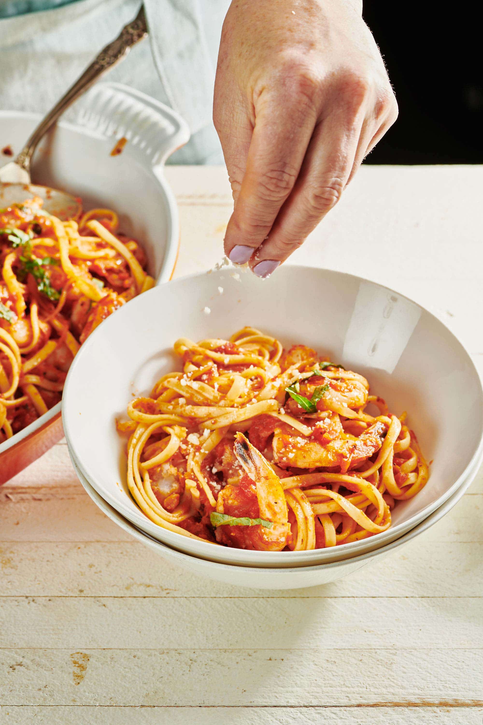 Woman sprinkling Parmesan over bowl of Shrimp Fra Diavolo with Linguine.