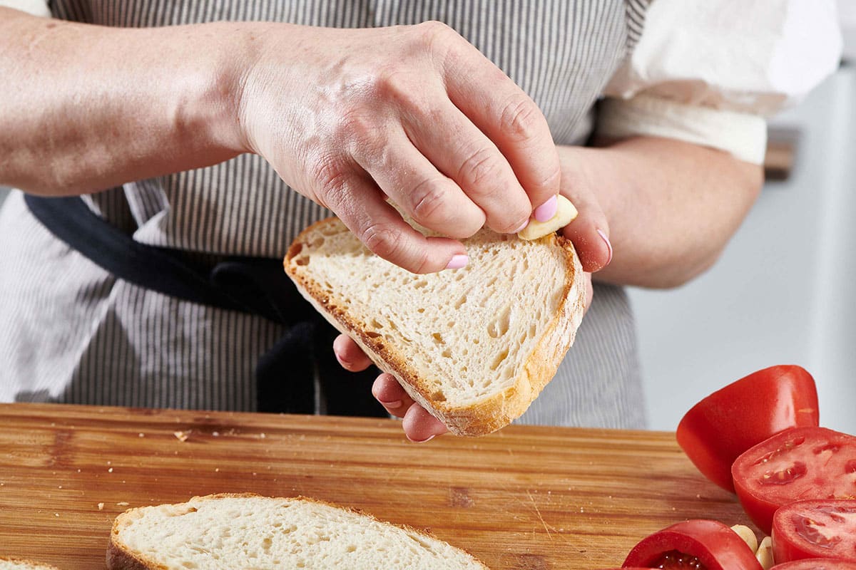 Woman rubbing garlic on a slice of bread.