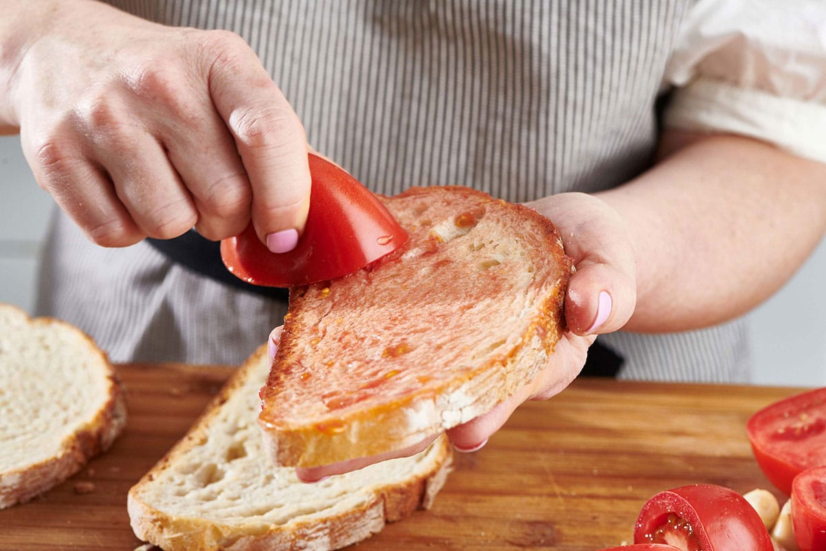 Woman rubbing a cut tomato on a slice of bread.