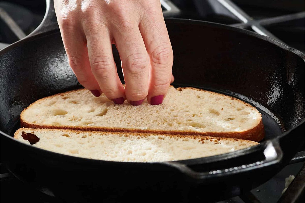 Woman toasting sliced bread in cast iron pan.