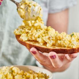 Woman spooning egg salad on bread.