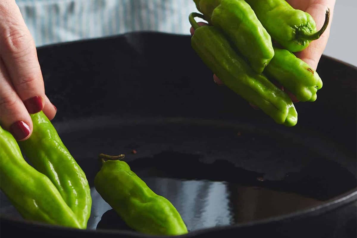 Woman putting Shishito Peppers into a skillet.