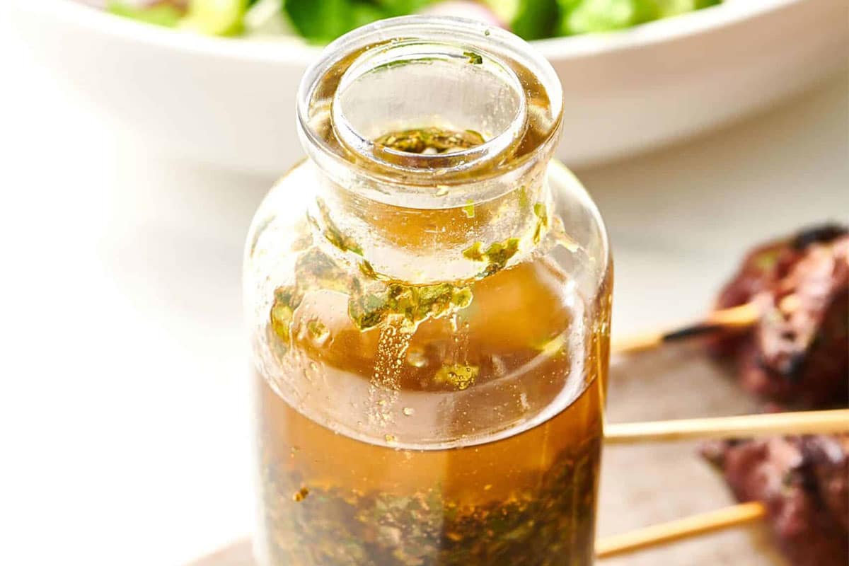 Glass jar of Chermoula next to skewered meat.
