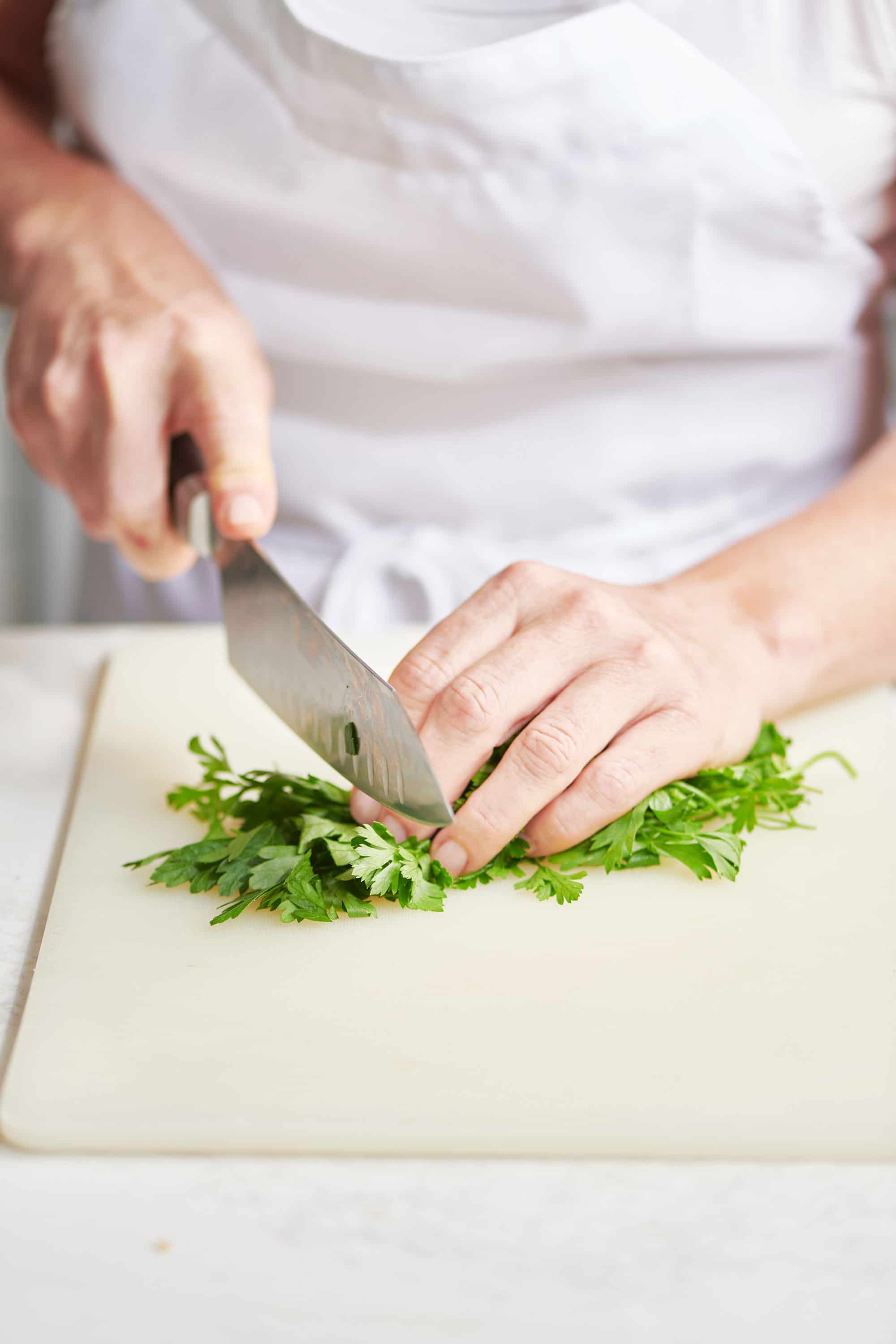 Chopping parsley on cutting board with chef knife.