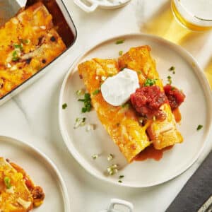 Enchiladas on plates with toppings and drinks.
