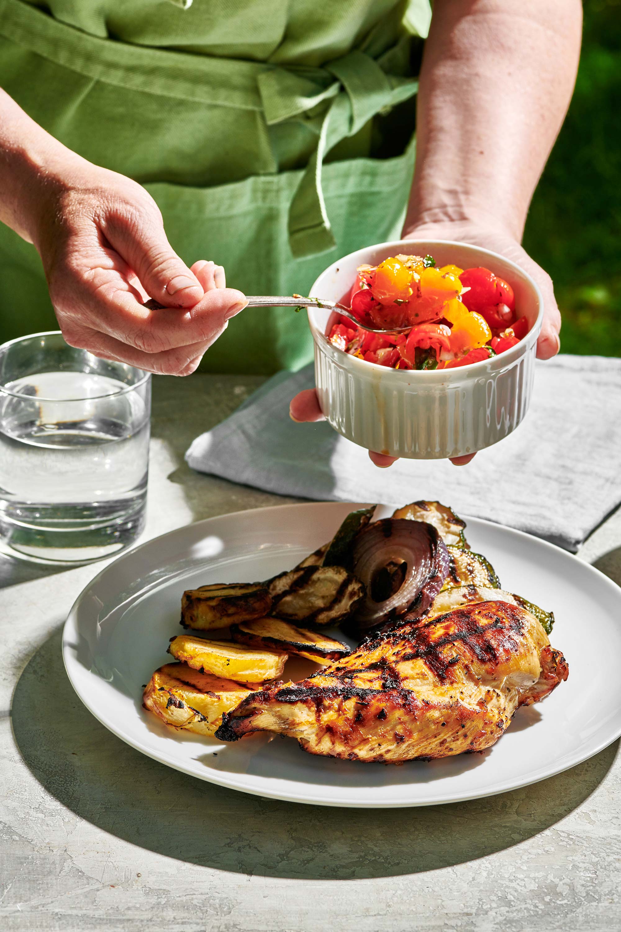 Woman scooping tomatoes onto a plate with a Grilled Chicken Breast.