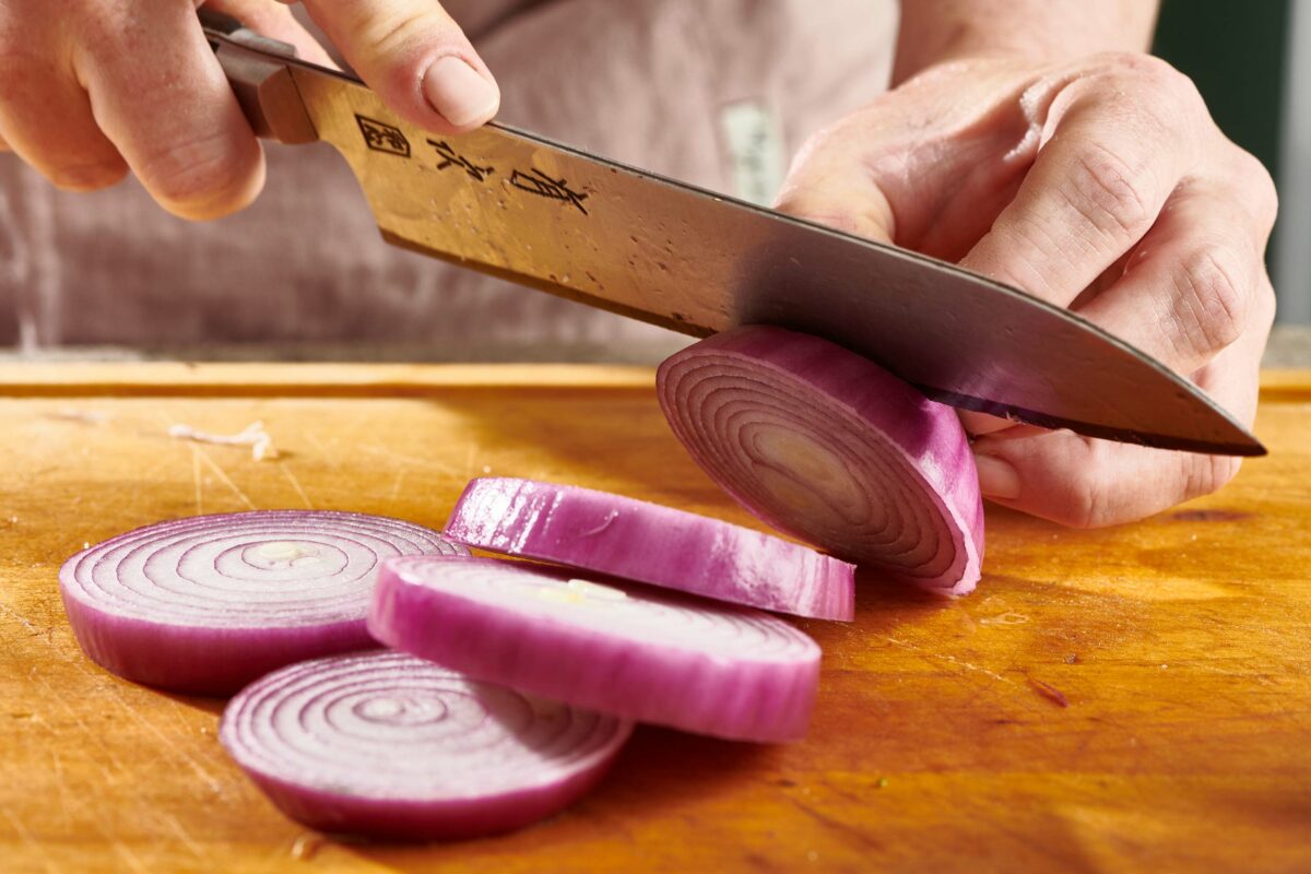 Woman slicing red onions with a large knife.