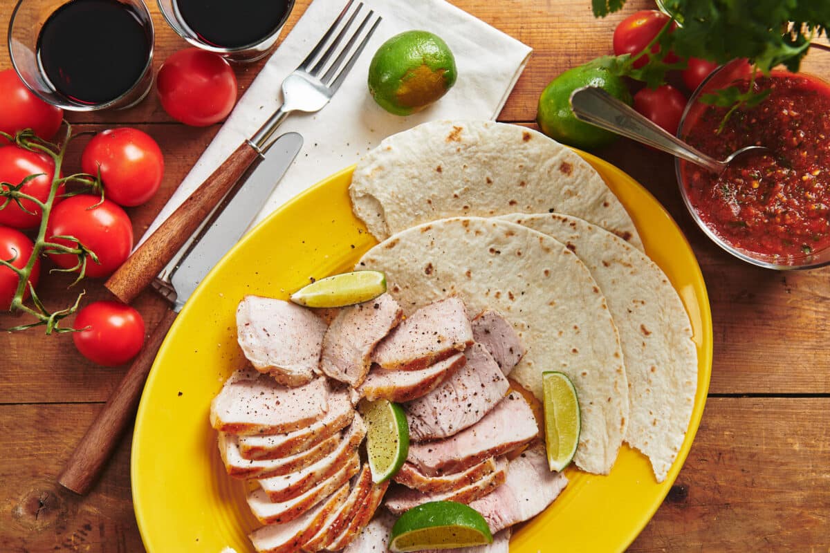 Plate set with tortillas and slices of grilled pork.