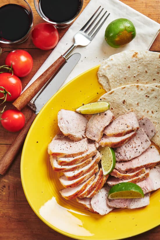 Slices of Grilled Pork and tortillas on a yellow plate.